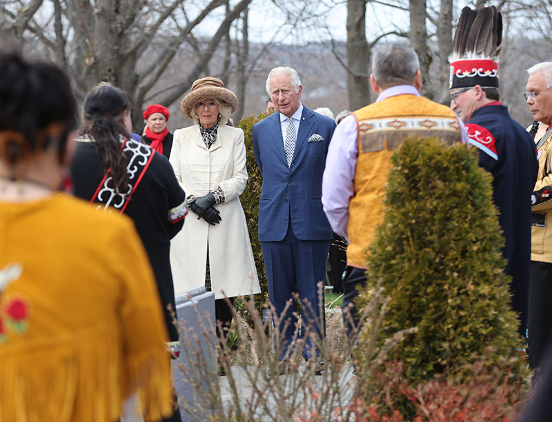 The Prince of Wales and the Duchess of Cornwall are standing with Indigenous leaders, in a solemn moment.