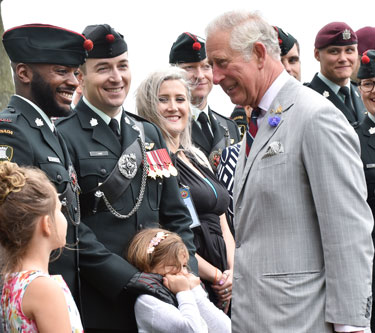 King Charles III stands and smiles at people wearing a black military uniform.