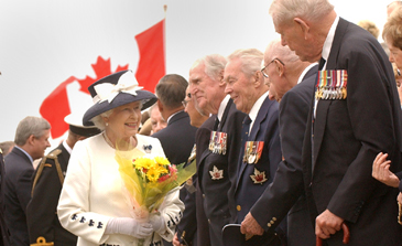 Queen Elizabeth II is smiling in front of a row of World War II veterans.