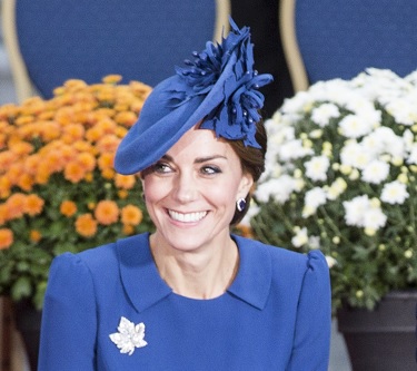 La princesse de Galles sourit à la caméra. Elle porte une robe et un chapeau bleu. Une broche en feuille d'érable est posée sur sa robe.