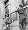 Two soldiers hang a sign for the Maple Leaf newspaper, 1944.