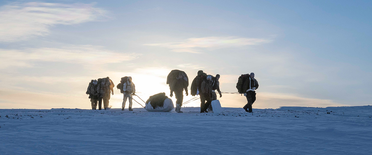 A small group of Canadian Armed Forces personnel carrying equipment across Arctic tundra