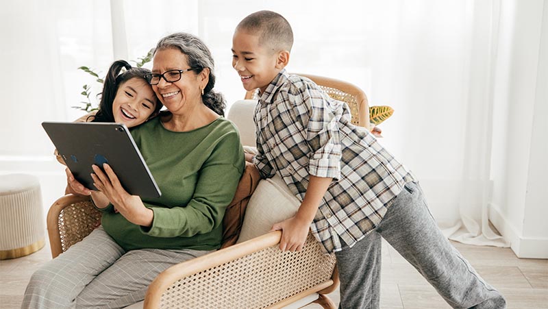 An older woman and two children smiling while looking at something on a tablet device
