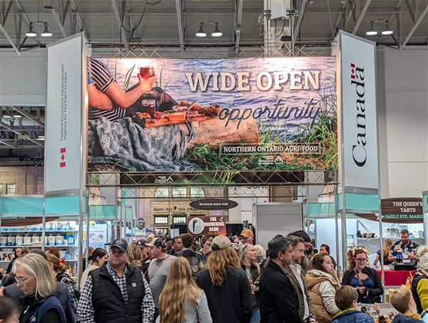 Une foule debout sous un panneau au pavillon agroalimentaire du Nord de l’Ontario. Sur le panneau est inscrit « Des occasions à perte de vue », avec le mot-symbole « Canada »