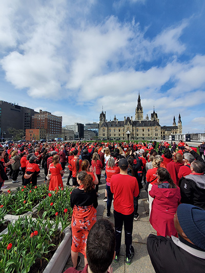 Une foule de personnes portant des chandails rouges. Les édifices du Parlement sont en arrière-plan