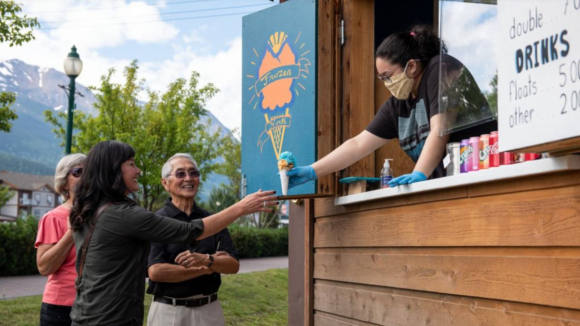 Image dans un stand de crème glacée, une employée donne un cornet de crème glacée à un groupe de clients.