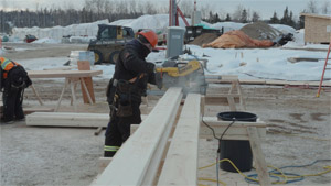 Un travailleur de la construction utilise une scie circulaire DeWalt sur un chantier; des équipements de construction sont visibles à l’arrière-plan