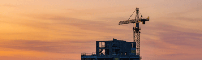 Le sommet d’un bâtiment en construction et le sommet d’une grue de construction statique de grande hauteur sont visibles contre l’arrière-plan d’un ciel illuminée par un coucher de soleil