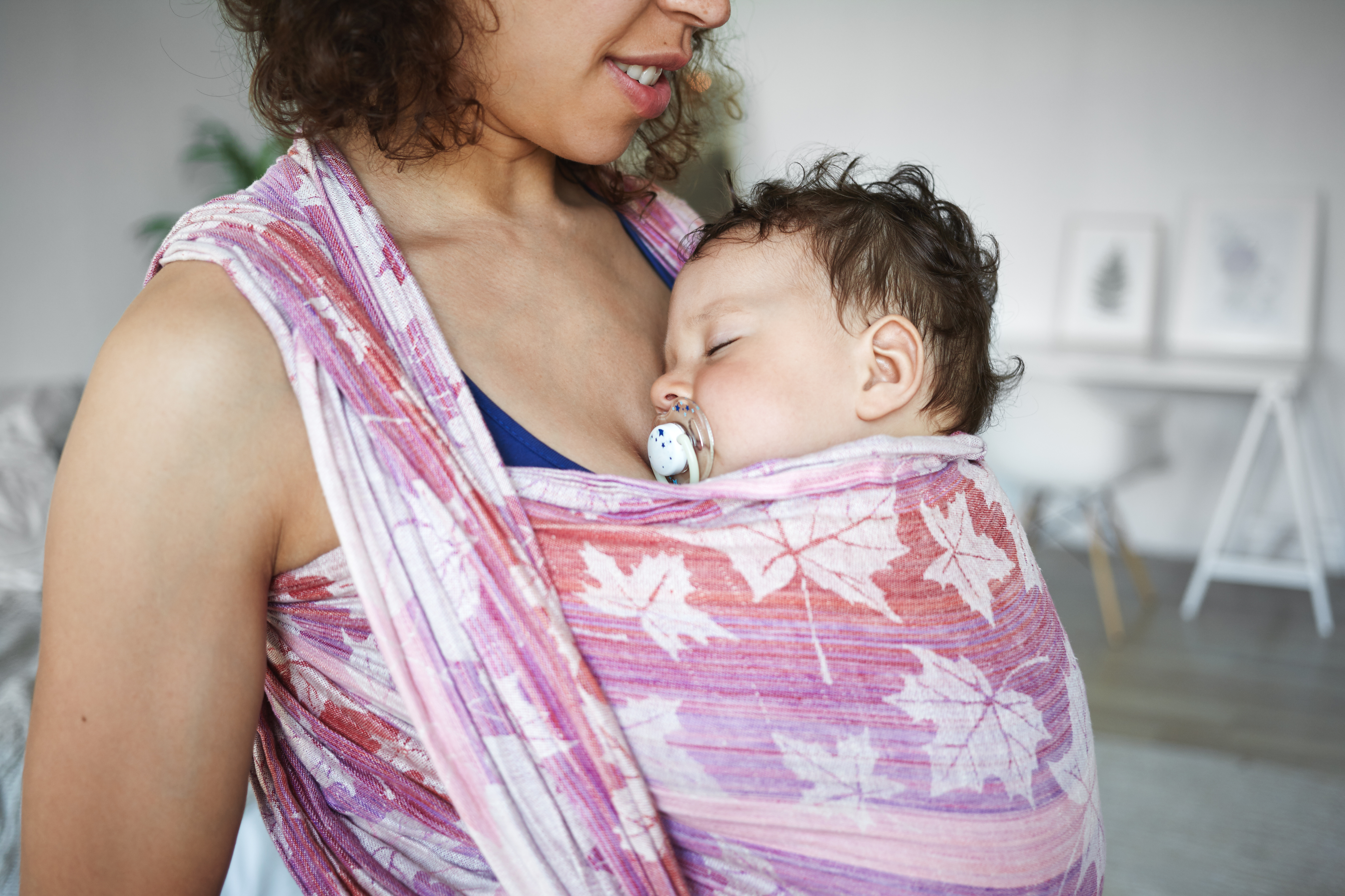 A parent wears their sleeping baby in a sling.