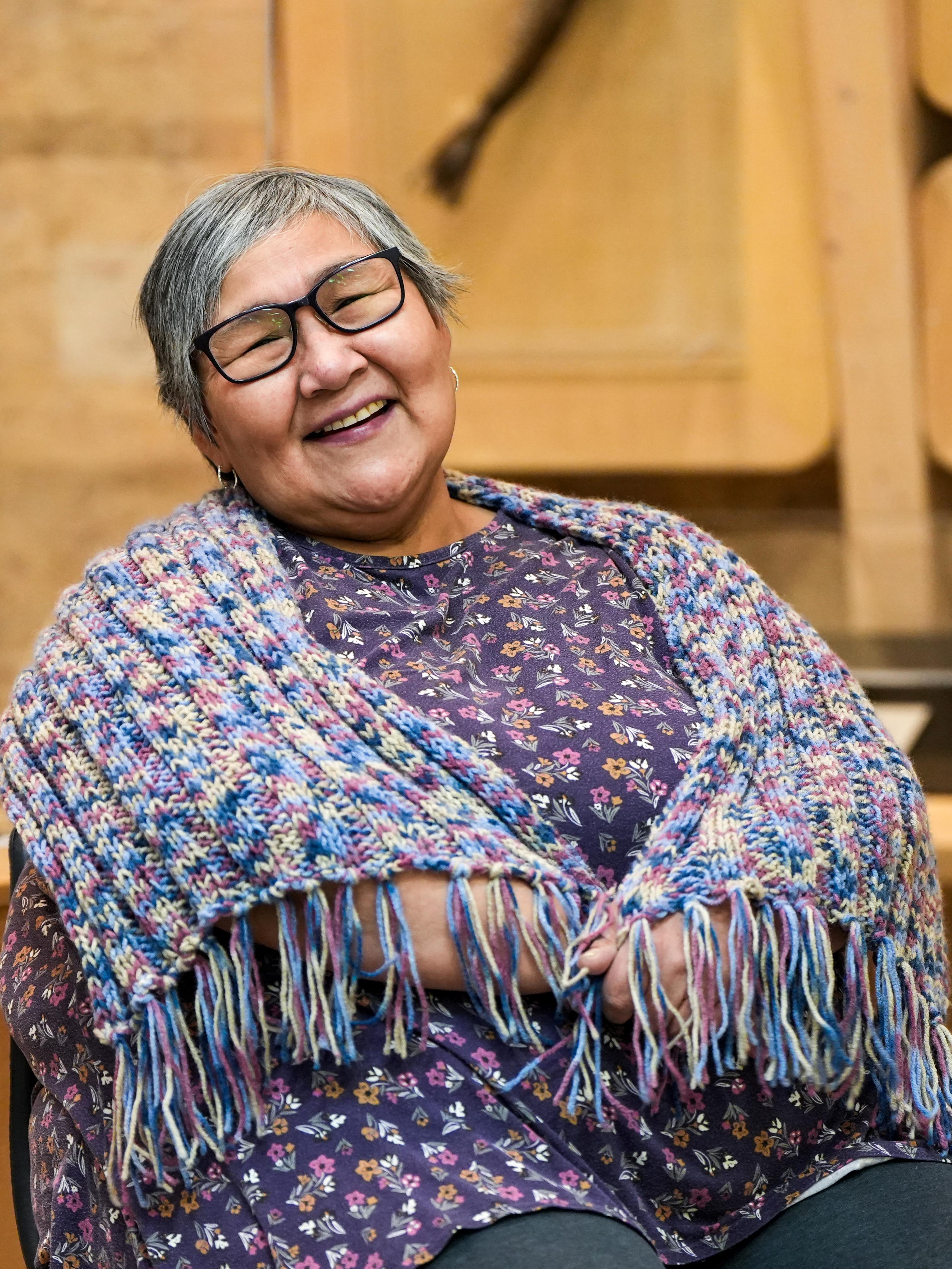 Woman, with knitted shawl around her shoulders, laughing.