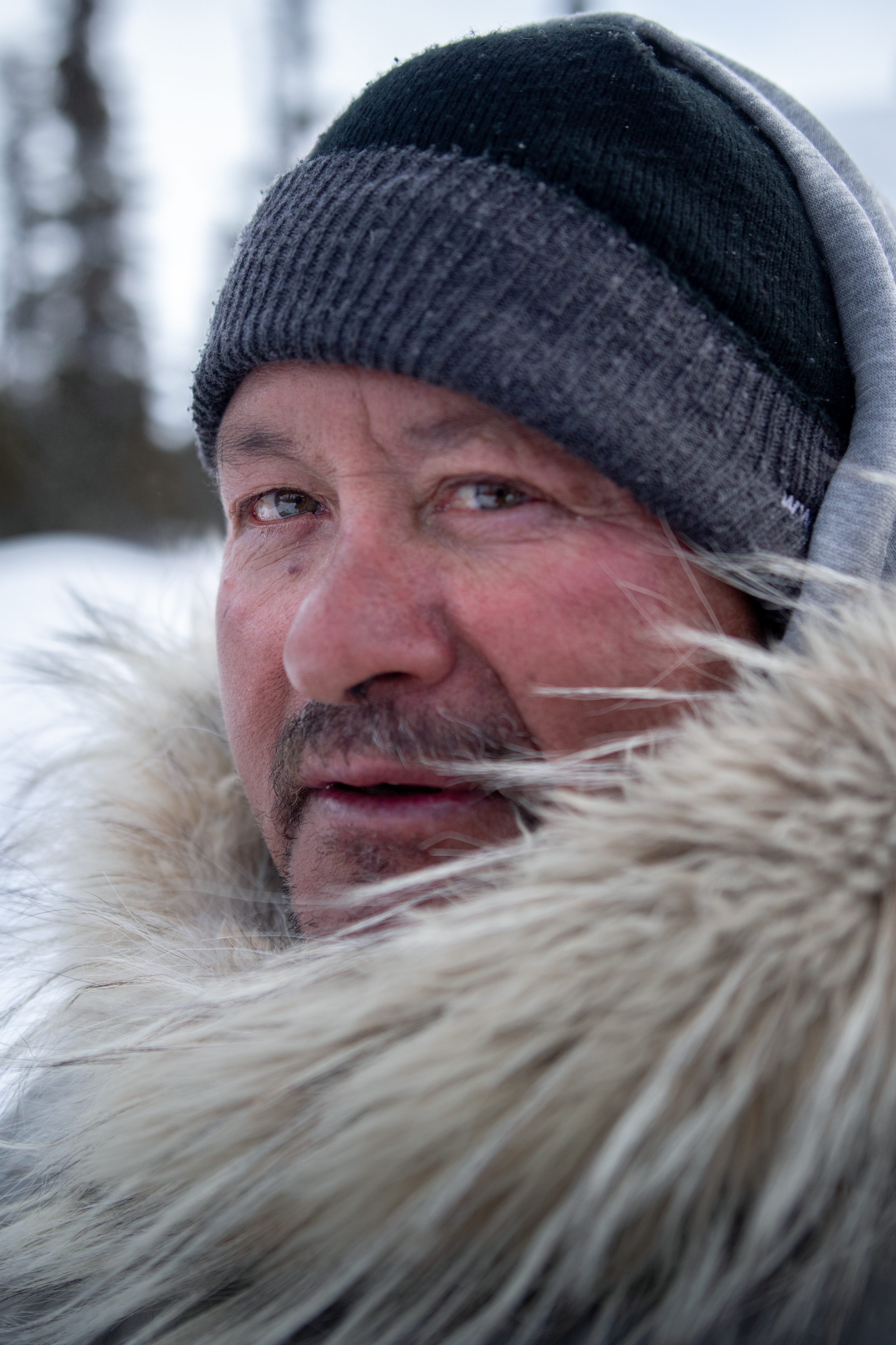 Headshot of man wearing knitted hat. His face is surrounded by large fur ruff on his hood.