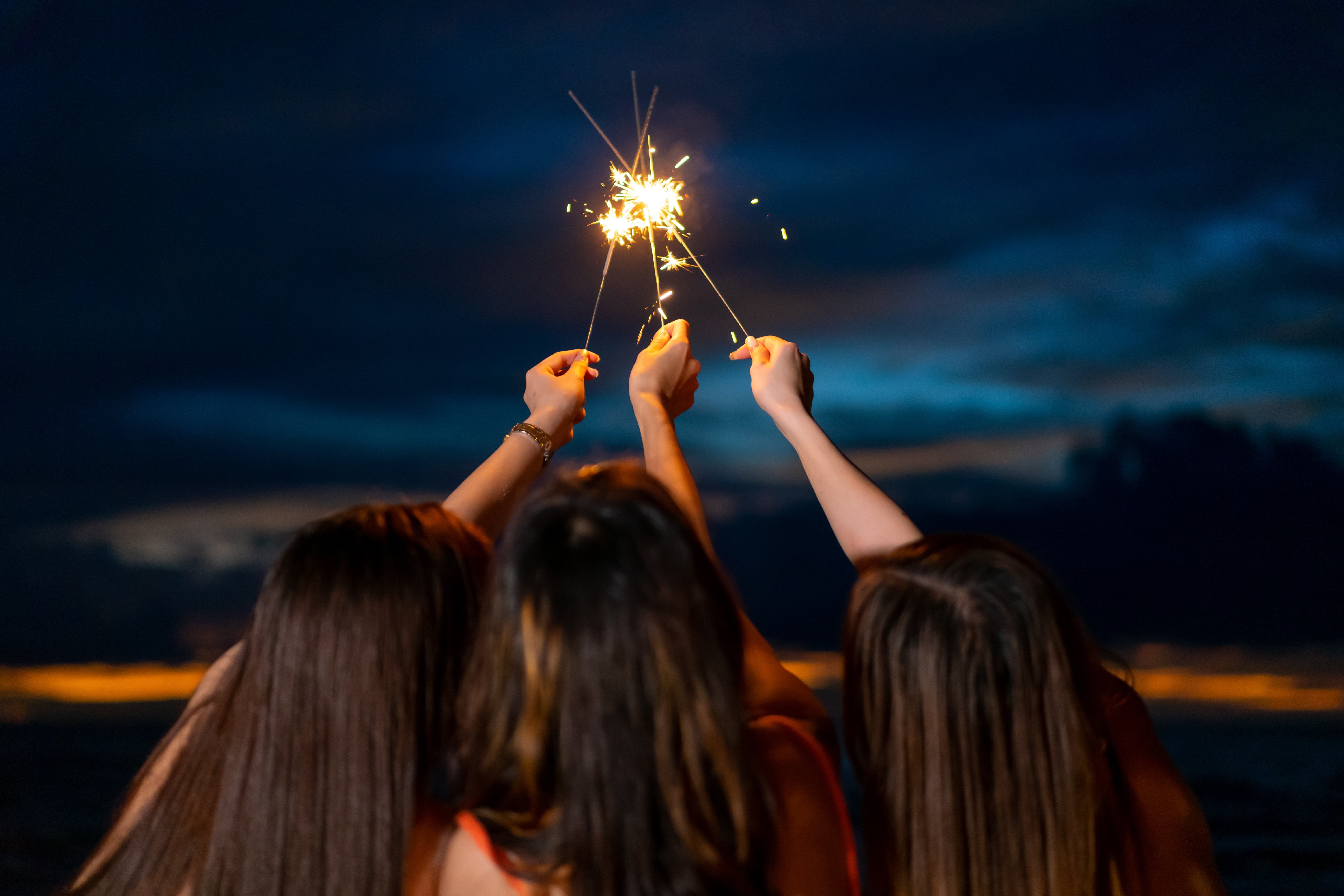 Photo –Three hands holding lit sparklers.