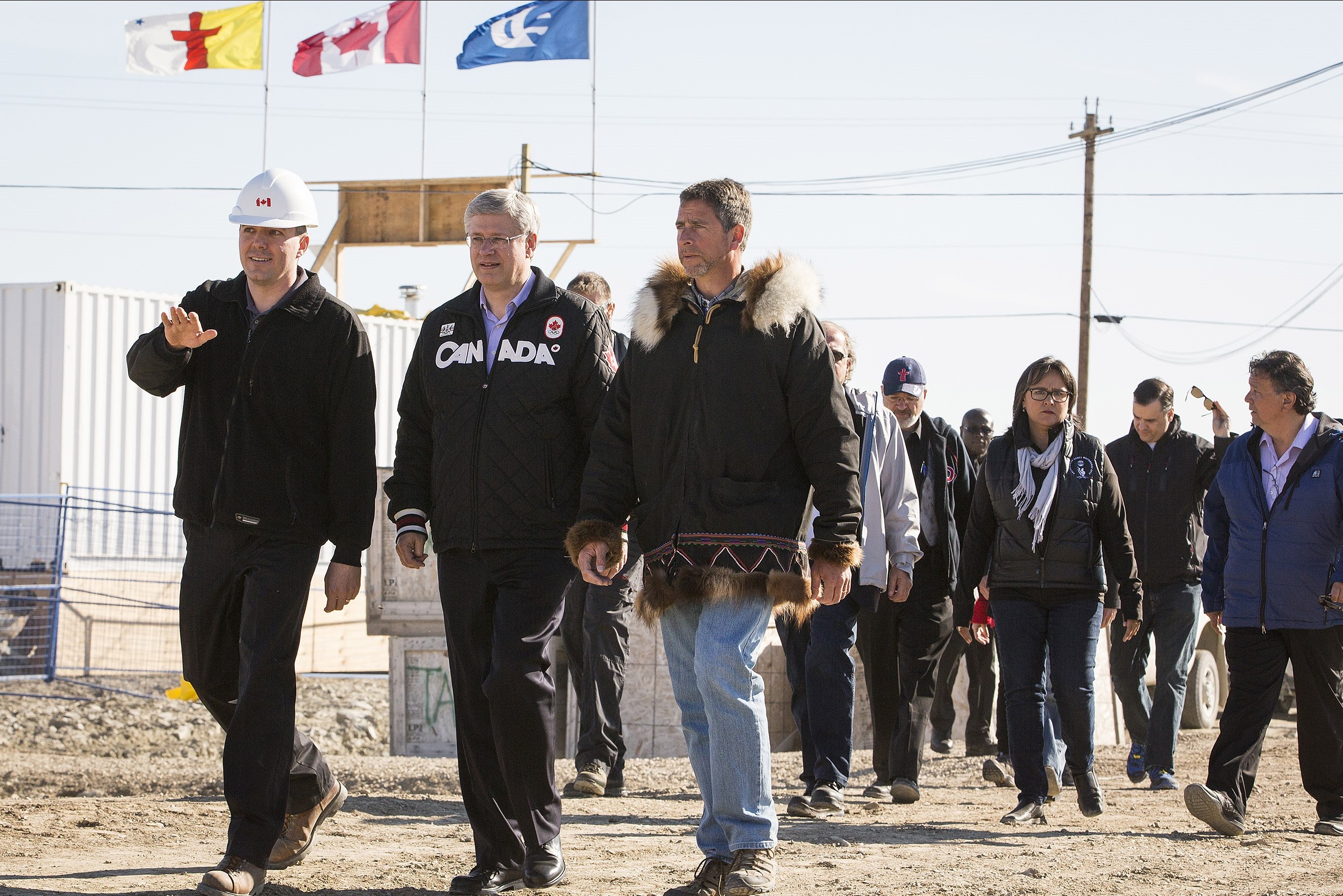 Photo – Three men walking outdoors. Former Prime Minister Stephen Harper is in the middle.