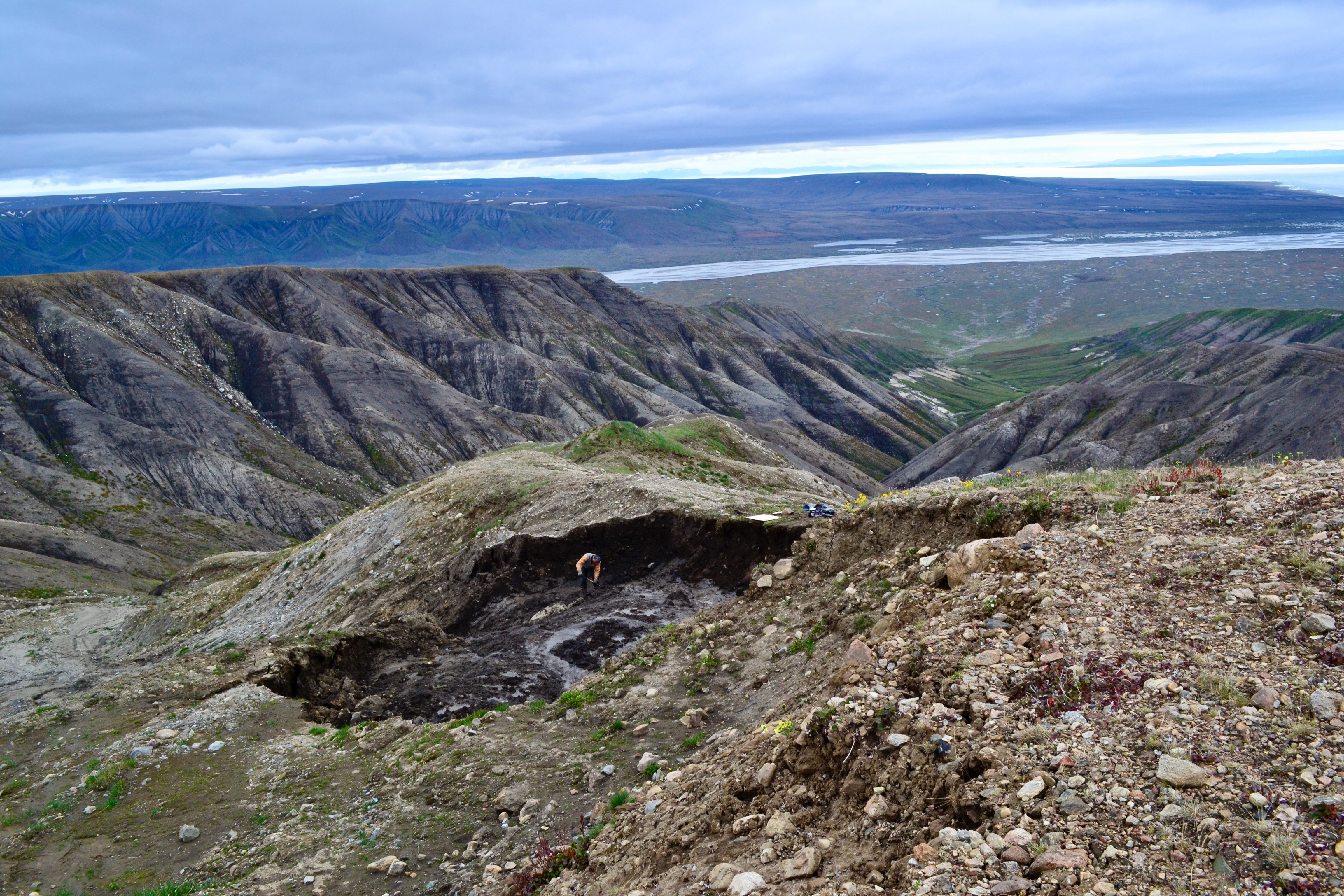Scenic view of rugged, treeless hills. In the foreground, a person digs in ice on a section of hill that has collapsed.