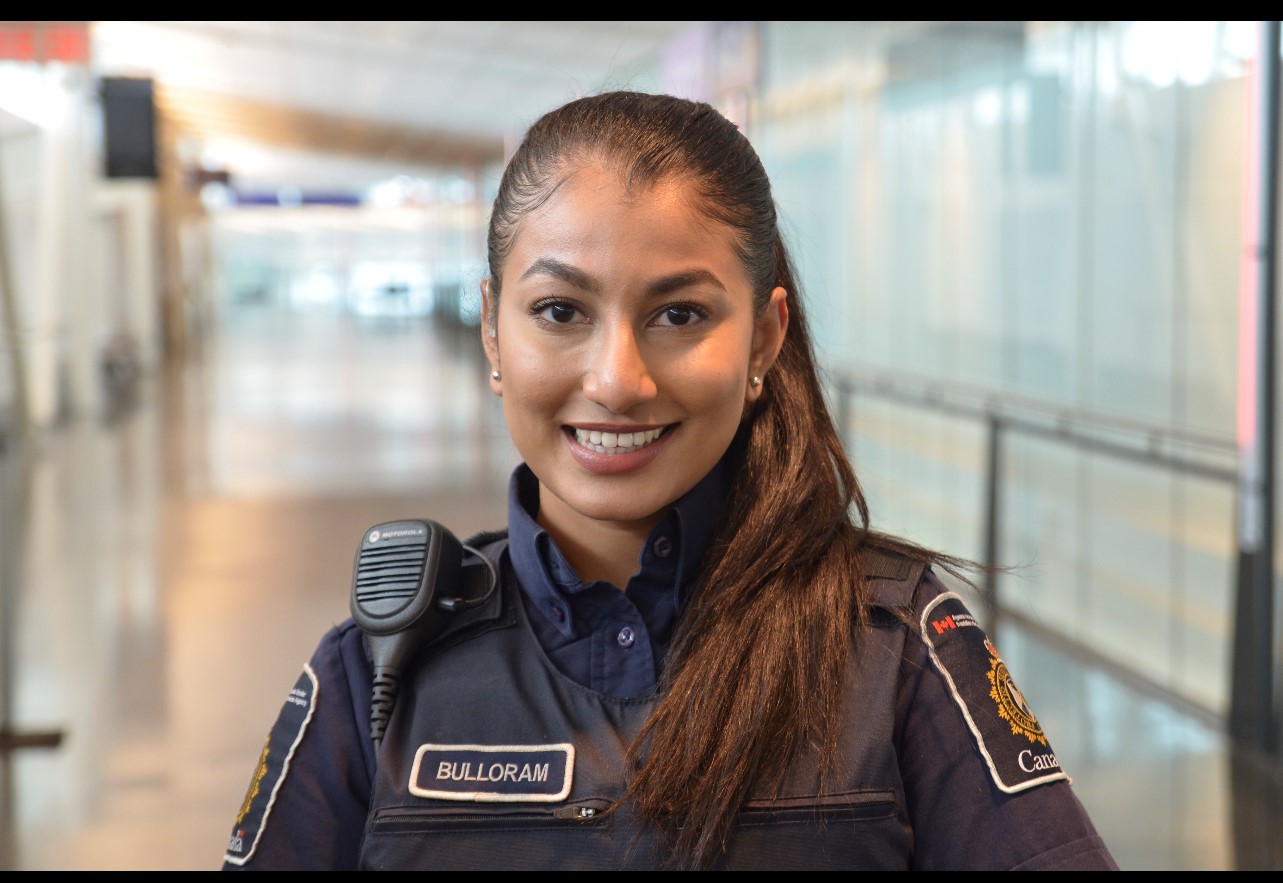 Une jeune étudiante agente des services frontaliers en uniforme, souriante, devant un arrière-plan flou.