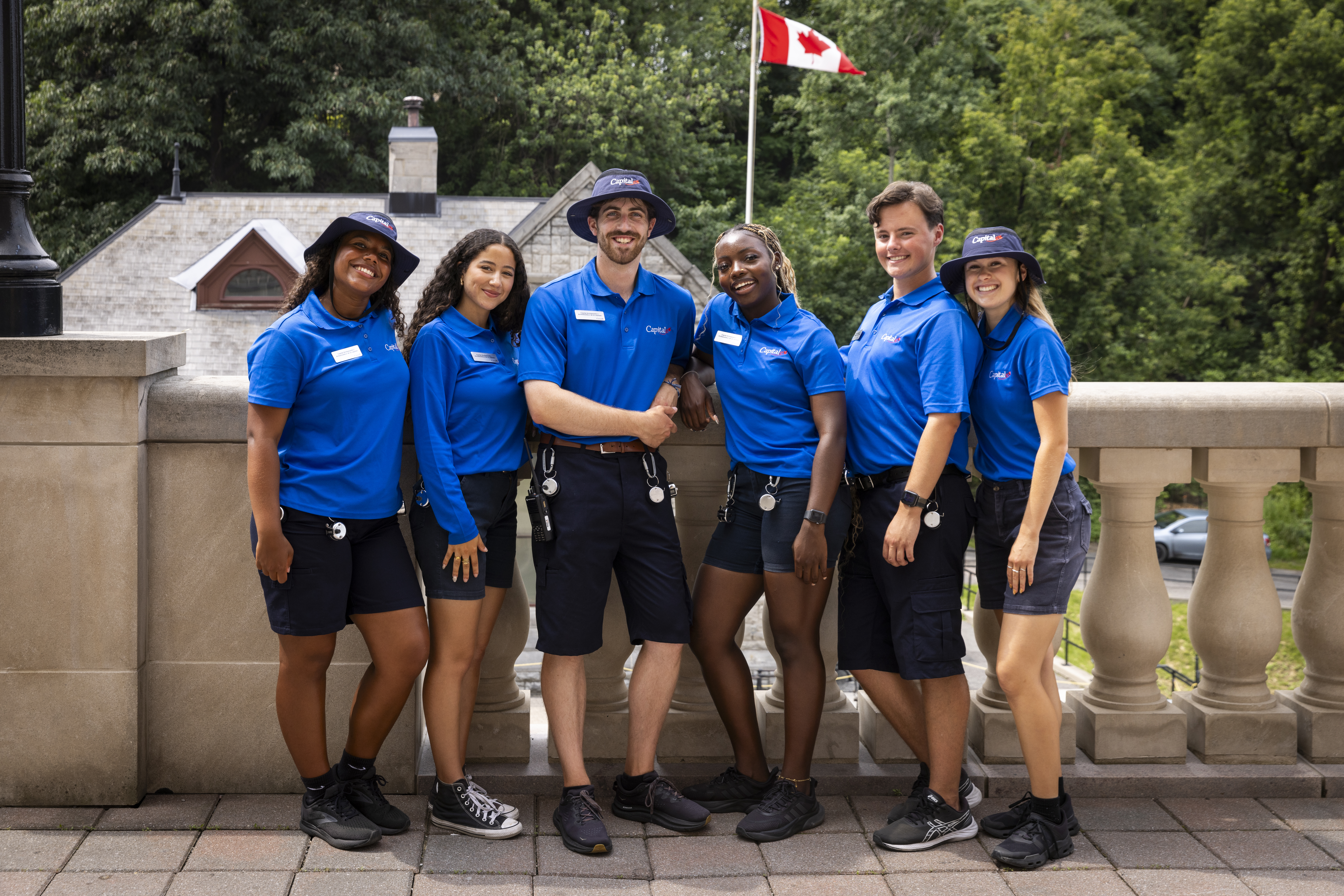 Six smiling young adults in blue uniforms, with a historic building in the background.