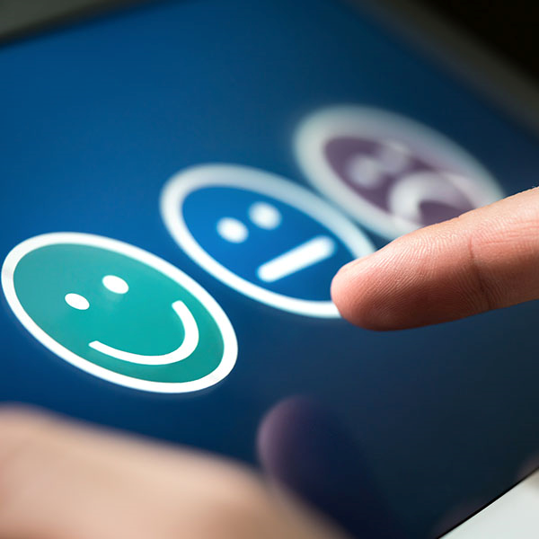 Close-up of finger pointing at smiling, neutral and sad emoticons on screen