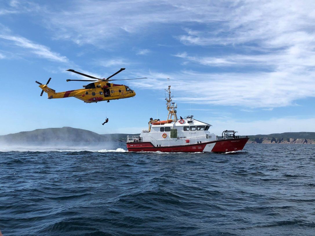 Yellow rescue helicopter hovers over ocean near the Canadian Coast Guard Ship Pennant Bay as part of search and rescue training