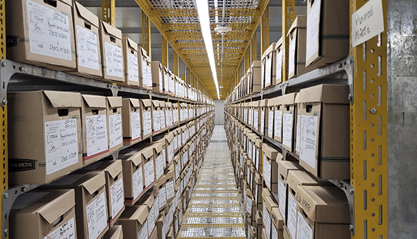 A long aisle in a warehouse with cardboard boxes stacked on steel shelves on each side.
