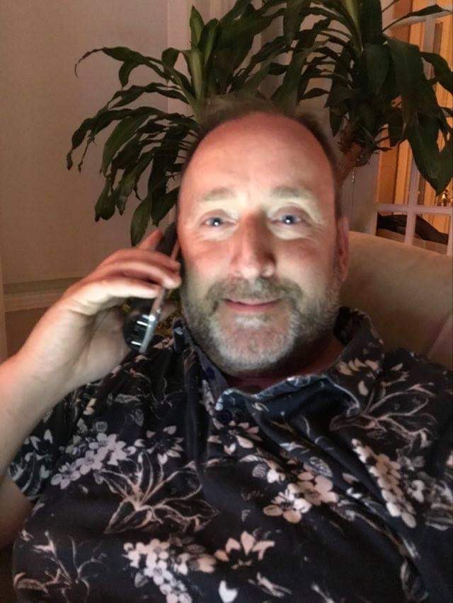 Alain Dorion speaking on a phone and smiling is sitting in a chair.