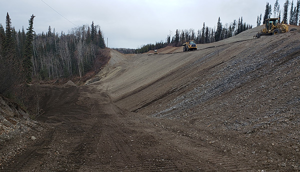 Tractors working on a road at the top of a sandy slope