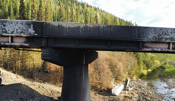 A closeup of a bridge in a forested area, with blackened concrete from fire damage