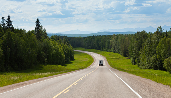 Route entourée de verdure et d'un ciel bleu, sur laquelle une voiture roule au loin