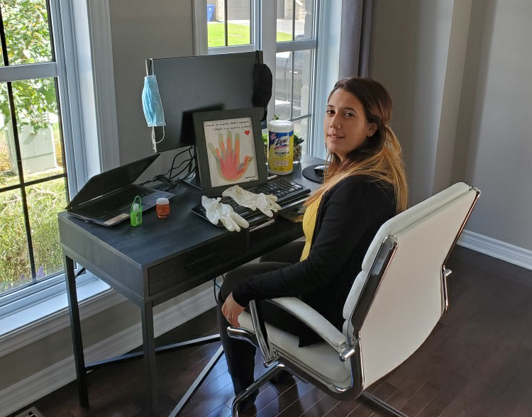 Amanda Assi is sitting in a chair. In front of her is a desk with various pieces of personal protective equipment, such as gloves and a mask.