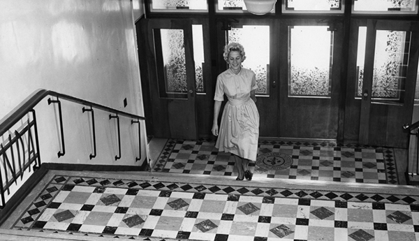 Photo d'archives en noir et blanc montrant une femme qui monte un escalier dans un immeuble ancien.