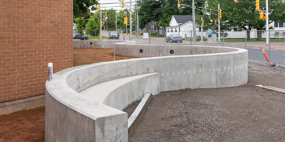 Construction of a curved concrete wall facing a red brick building