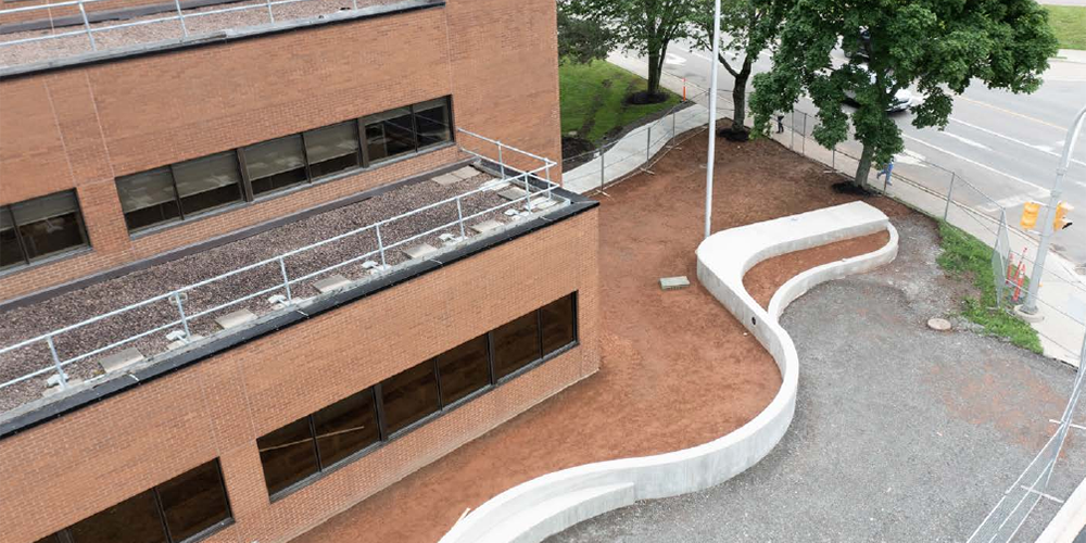 Low curved concrete wall on clay bordering a red brick building