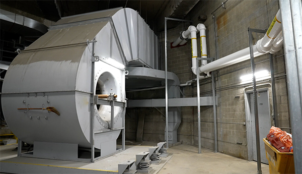 Gros cylindre métallique à côté de tuyaux blancs dans une salle mécanique en béton.