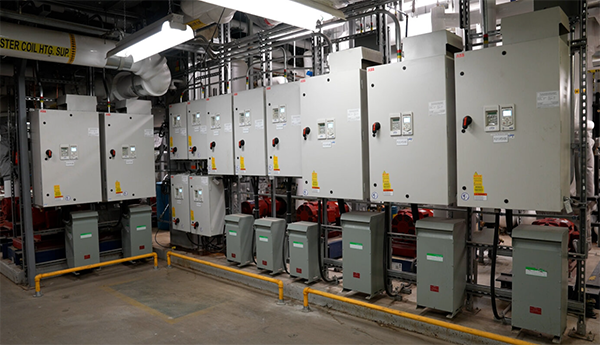 Une rangée de petites boîtes métalliques en dessous de plus larges boîtes grises suspendues dans une salle mécanique.