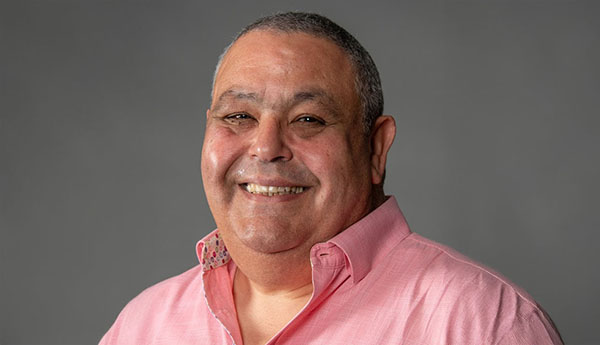 Un homme souriant portant un chandail rose.