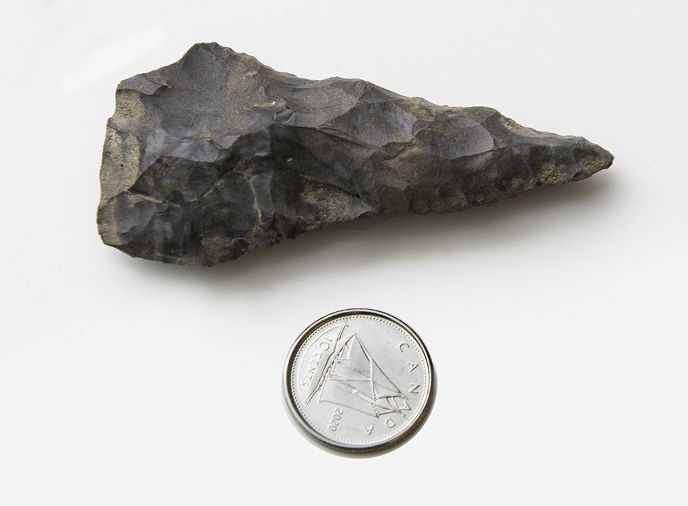 A dime next to a carved, pointed stone.