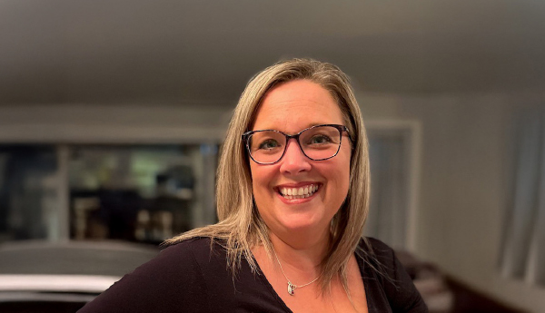 Portrait of a smiling woman with medium-length hair wearing glasses and a dark sweater.