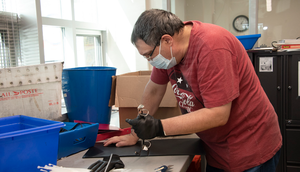 Masked person dismantling a black binder on a desk.