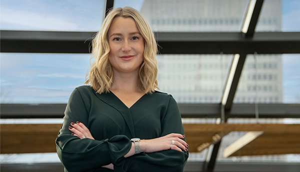 Une jeune femme est debout, les bras croisés, sous un grand puits de lumière.