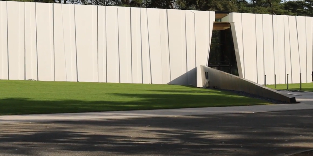 The exterior of a white rectangular building, with a triangular entrance and a green lawn.