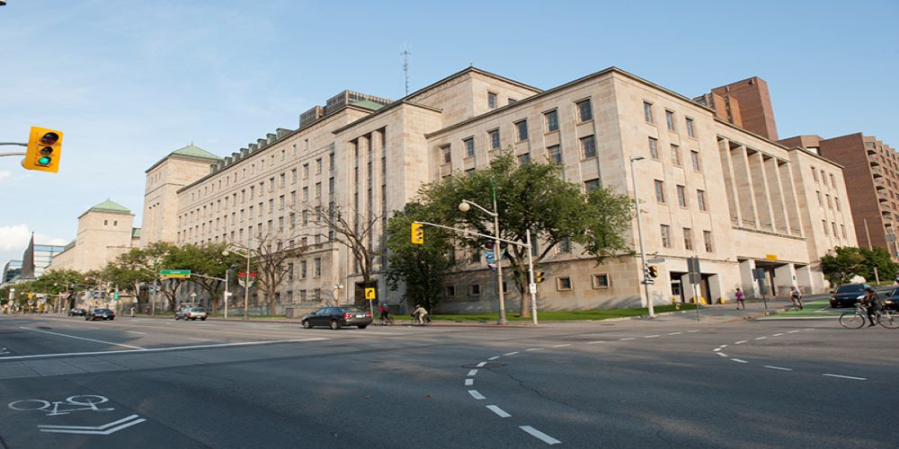 A large heritage building on a street corner, with trees in front of it.