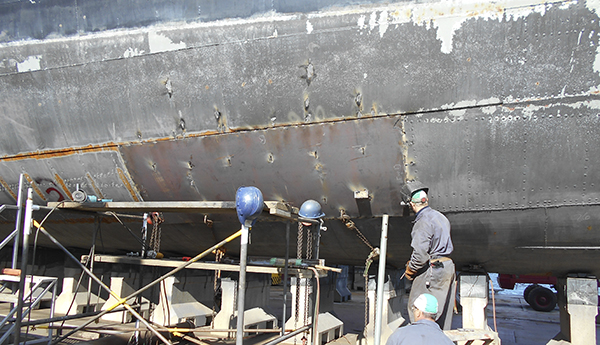 People working on fixing the corroded steel plates of a ship's hull.