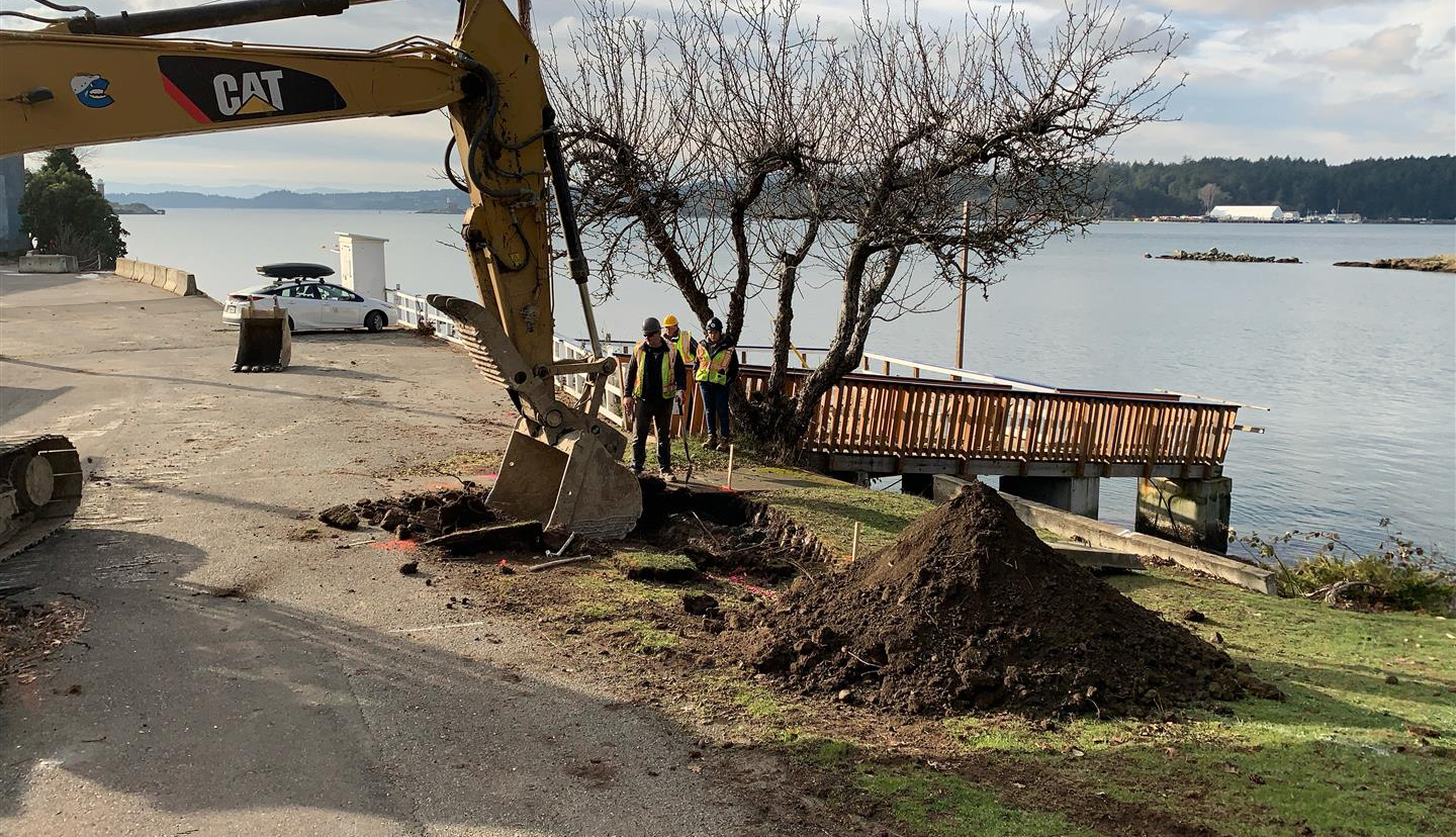 Des machines d’excavation creusent un trou dans le sol près d’un rivage.