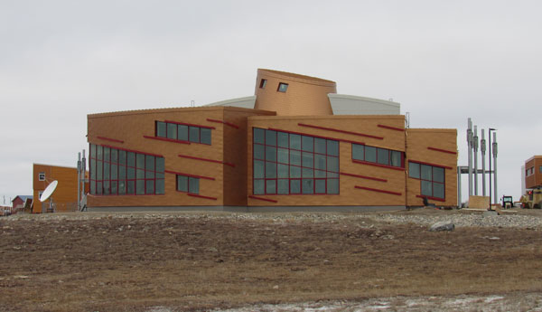 Three-section copper-coloured building with big windows, a small dome on the roof and vacant land in front