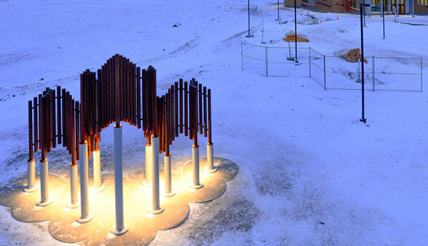 Bird's-eye view of a copper lighted maple leaf structure with a building in the back and a city behind it