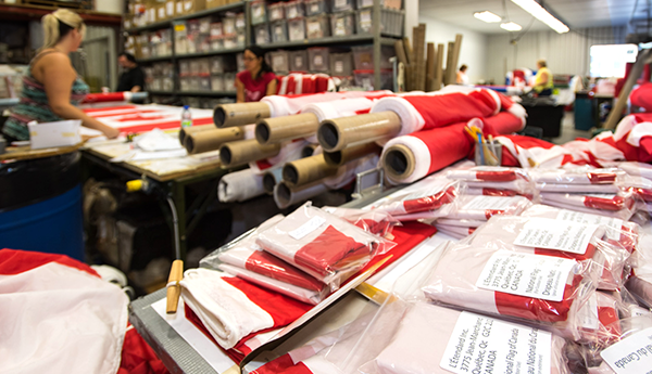Rolls of red and white fabric on a table. Transparent bags containing Canadian flags are in the foreground.