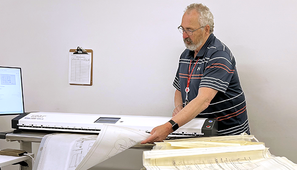 Man holding very large sheets of paper and digitizing them using a white horizontal device.