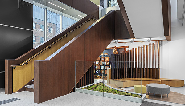 Escalier massif en bois brun dans une grande pièce blanche, où il y a une fenêtre et un endroit où s'asseoir à l'arrière-plan.