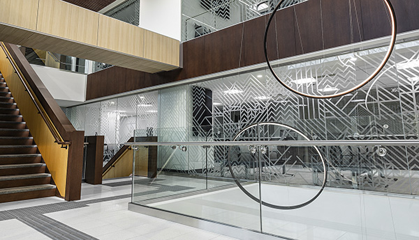 Plafond en lambris de bois et minces anneaux de bois suspendus dans un passage où il y a une barrière en verre. 
