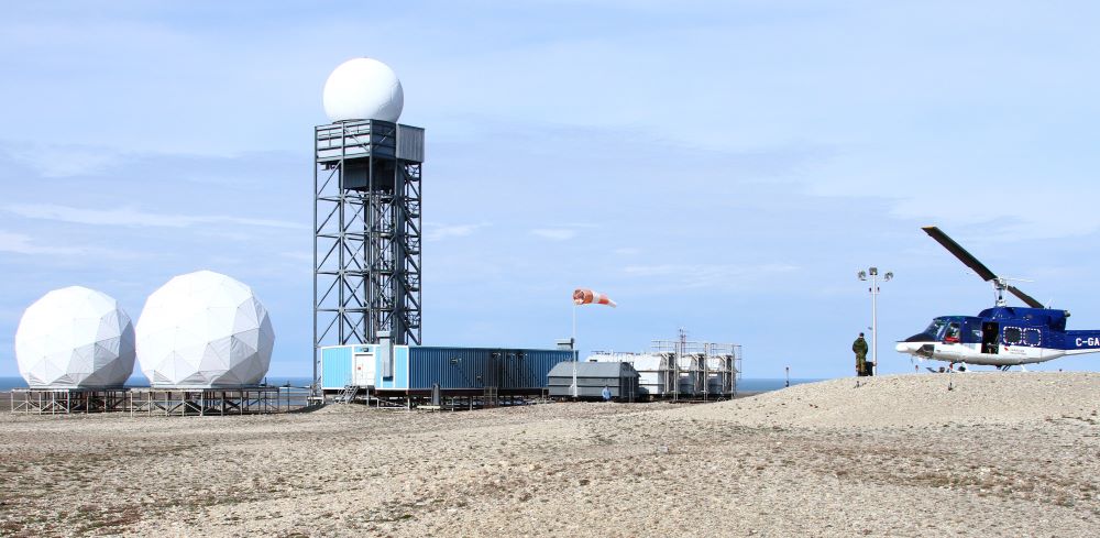 A sandy landscape with radar facilities in the background, along with a helicopter and soldier