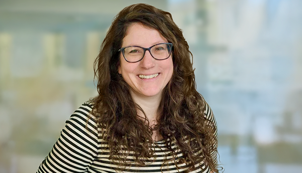 Centred view of a smiling woman with long curly hair wearing glasses.